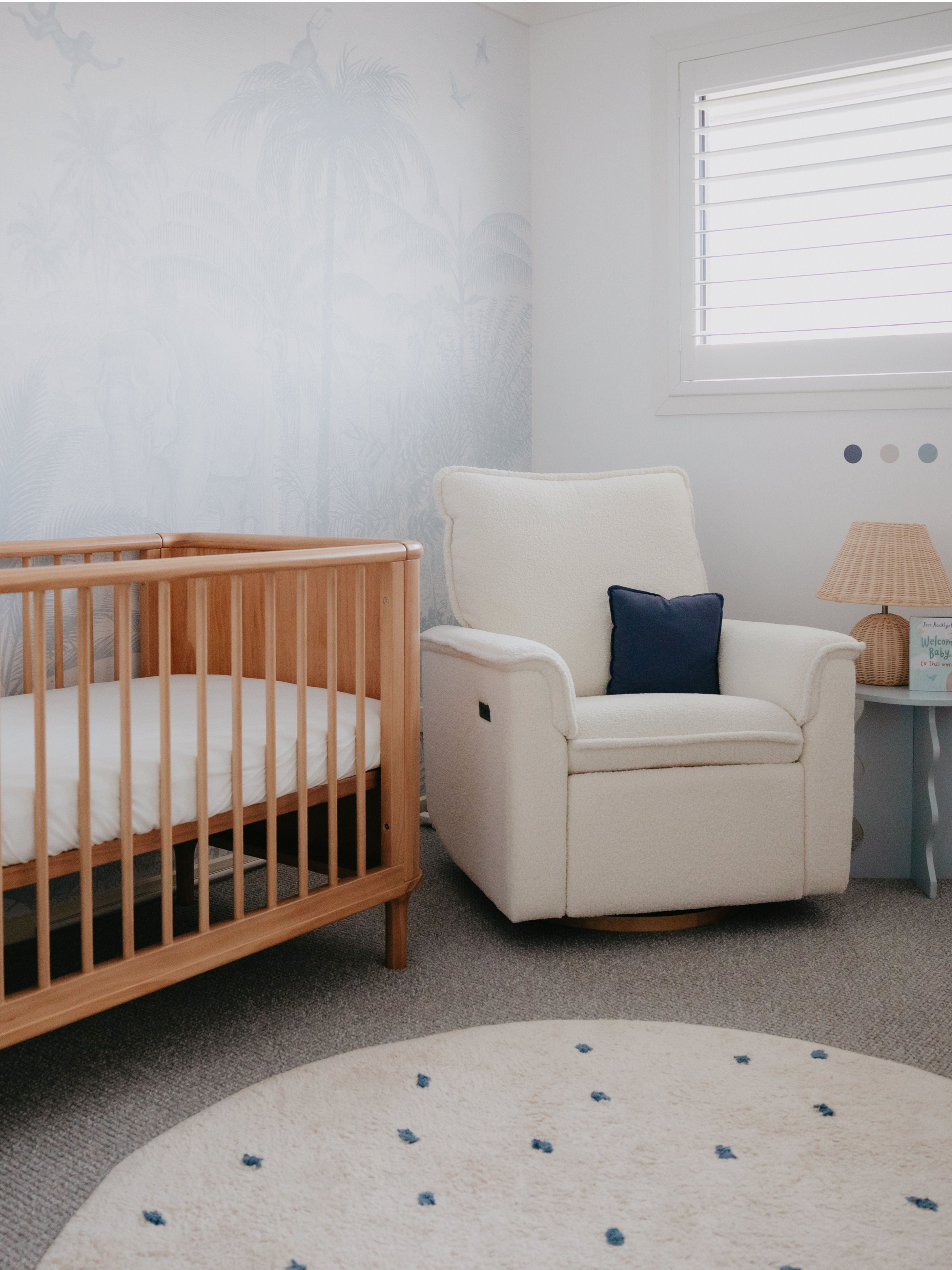 Nursery room with wooden crib, beige armchair, and round rug.