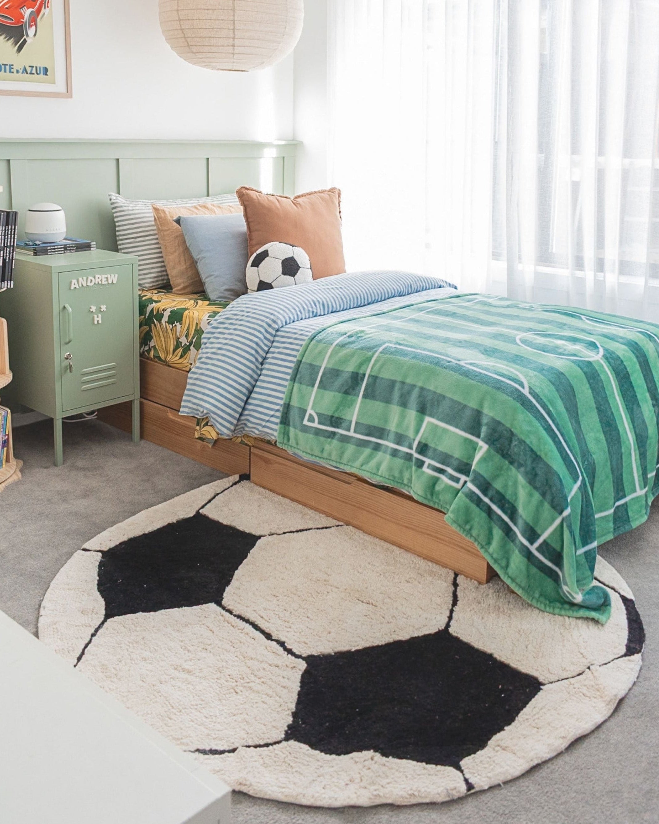 Children's bedroom with a soccer ball-shaped rug, bed with green and blue plaid blanket, and green locker.